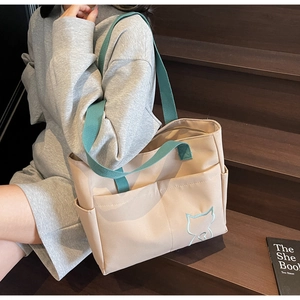 Detail of canvas tote bag with green straps and cat embroidery shown on stairs