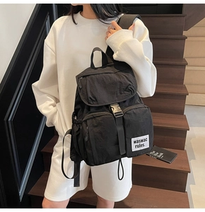 Detail view of black nylon backpack with two front square pockets and woven label on stairs
