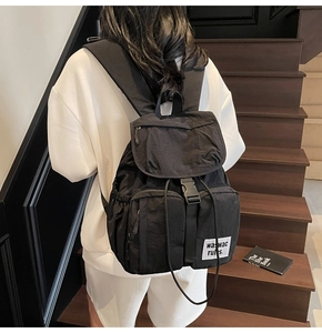 Detail of matte black nylon backpack with flap buckle and drawstring closure on stairs