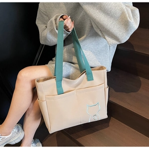 Detail of canvas tote bag with contrast green straps and cat embroidery on wooden steps