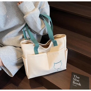 Detail of canvas tote bag showing green cat embroidery and functional side pockets