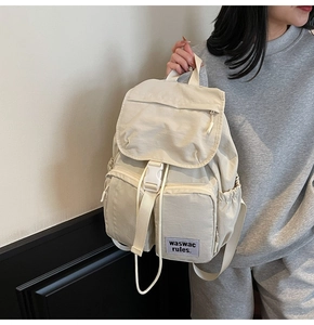 Detailed close-up of a cream nylon backpack with buckle flap and multiple zip pockets