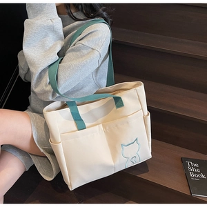 Detail of canvas tote bag featuring green straps and blue cat embroidery on stairs