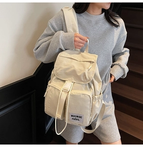 Close-up of beige nylon travel backpack showing multi-pocket design and flap closure detail