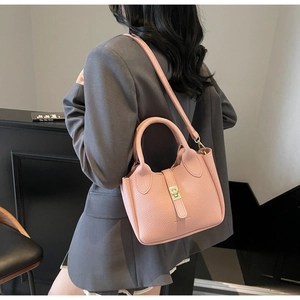 Detail view of pink lychee leather bucket bag with gold metal lock on a female model