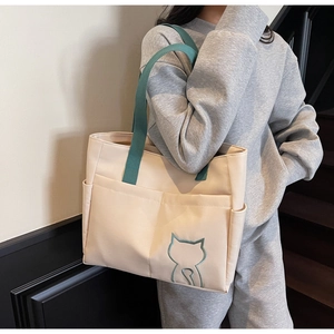 Detail of large canvas tote bag with green straps and minimalist cat embroidery detail