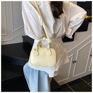 Detail of light yellow retro crossbody bag with embossed lettering and silver hardware