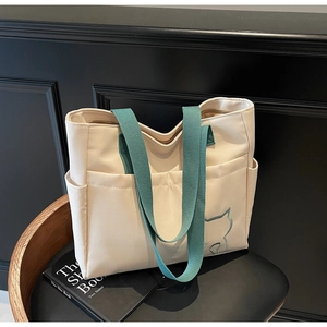 Detail view of canvas tote bag featuring cat embroidery, front pockets, and green handles