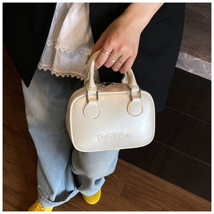 Detail shot of a cream leather Boston bag featuring an embossed RETRO logo and dual handles