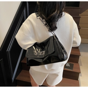 Close-up of black glossy leather tote bag with metal chain strap worn by a model