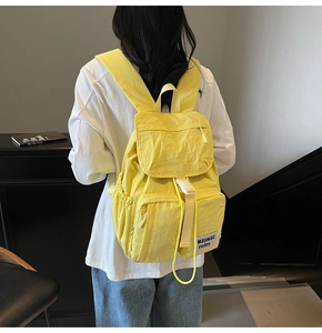Rear view of model wearing a bright yellow multi-pocket travel backpack with buckle closure