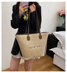 Detail of woven straw tote bag with brown leather handles and Tote Bag embroidery