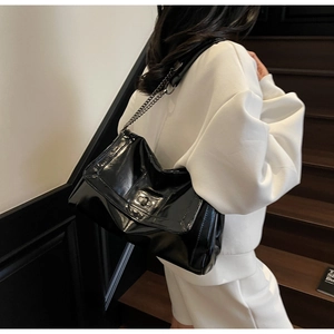 Detail of black glossy leather tote bag with metallic chain strap and twist-lock on model