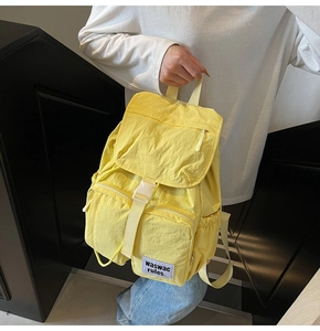 Detail view of yellow nylon backpack featuring buckle closure and brand label