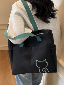Black tote bag with green straps and cat embroidery shown on model in home setting