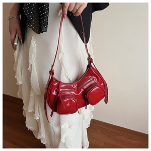 Detail of red glossy crescent shoulder bag with multi-pocket design and metal zippers