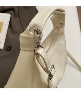 Close-up of matte cream leather handbag showing knotted handle and silver metal hardware hook