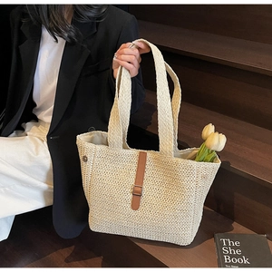Détail d'un sac cabas tissé beige avec bandoulière en cuir marron et boucle sur des escaliers