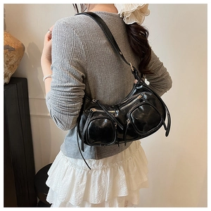 Detail of a black shiny patent leather punk shoulder bag with zippers on a female model