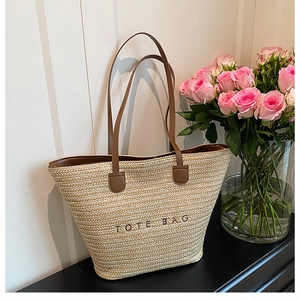 Close-up of straw tote bag featuring TOTE BAG embroidery and deep brown handles