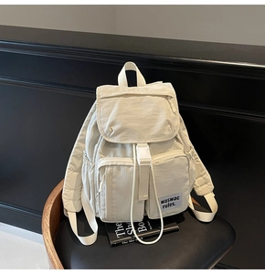 Detail view of a cream minimalist nylon backpack with multiple front pockets and buckle closure