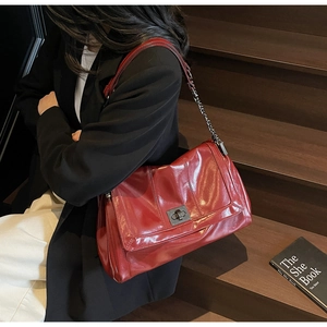 Detail of dark red glossy leather tote bag featuring a metallic turn-lock and chain strap