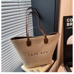 Detailed close-up of woven straw tote bag featuring embroidered text and leather handles