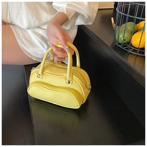 Detail of a bright yellow litchi pattern mini boston bag with double handles and zipper