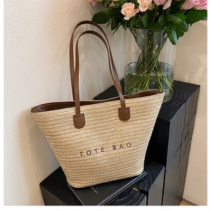 Detail of hand-woven straw tote bag with brown leather handles and embroidered text