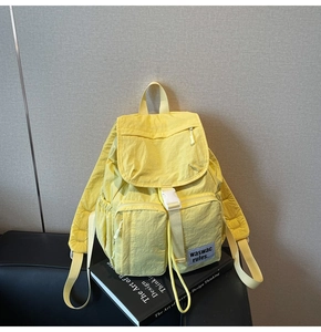 Detailed close-up of yellow lightweight nylon backpack with white buckle and side logo patch