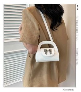 White fashion mini handbag with silver mirror bow detail shown on shoulder with long strap