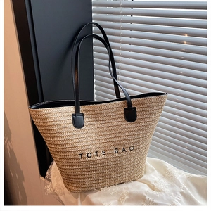 Detail of straw tote bag with black leather handles and TOTE BAG embroidery text