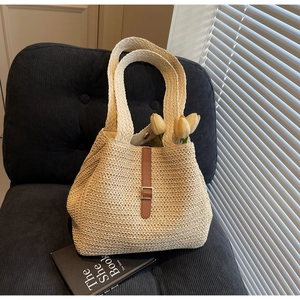 Détail du sac cabas en paille crème avec boucle en cuir marron et fermoir magnétique