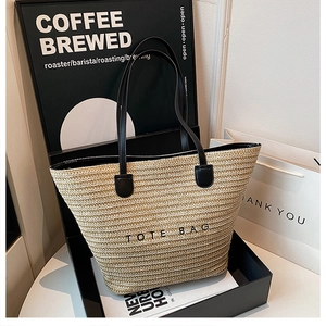 Detail view of woven straw tote bag with black leather handles and printed text in a gift box