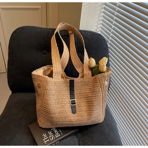 Détail d'un sac cabas en paille tissé avec boucle en cuir noir et fermoir magnétique