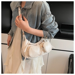 White crescent leather bag with functional pockets and golden zippers shown on a model