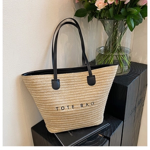 Detail of minimalist beige straw tote bag with black leather handles and TOTE BAG text print