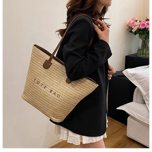 Detailed view of large straw tote bag with black embroidery and leather handles