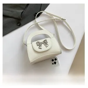 Detail view of mini cream crossbody bag with silver bow and leather texture