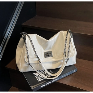 White glossy tote bag with metal chain strap on dark stairs next to urban books
