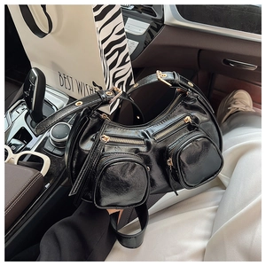 Detail view of black glossy patent leather biker bag with gold hardware in car setting