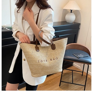 Close-up of beige woven tote bag with red embroidered lettering and brown leather handles