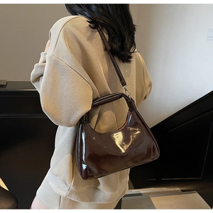 Detail of dark brown glossy patent leather shoulder bag with embossed brand logo
