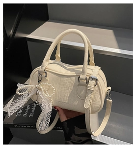 Detail of creamy white pillow bag with litchi texture and pearl bow charm accessory
