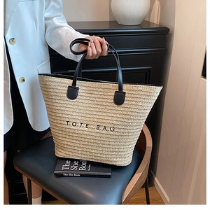 Detail of handwoven straw tote bag featuring contrast black leather handles and embroidered logo