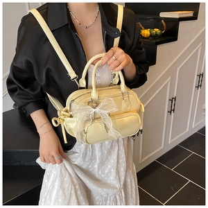 Close-up of cream yellow Boston bag with white mesh bow charm on indoor staircase