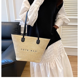 Detail of natural straw tote bag with black handles and embroidered text on textured fabric