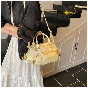 Detail of light yellow Boston bag with adjustable strap and lace bow charm on a model