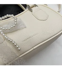 Detail of beige pebble leather handbag featuring pearl accents and white lace texture