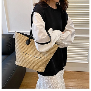 Detailed texture of woven straw tote bag featuring black TOTE BAG printed text and shoulder strap